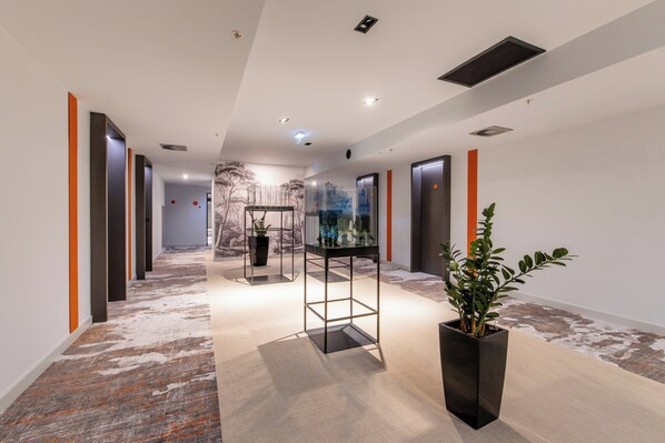 A modern hallway with a patterned carpet, a glass display case, and a potted plant. - Crowne Plaza Podgorica by IHG (Podgorica)