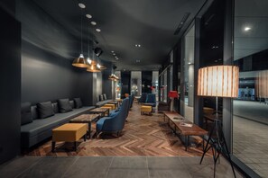 Un espacio lounge moderno con sofá, sillas azules, mesas de madera e iluminación colgante.