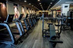 Un gimnasio con cintas de correr, máquinas de pesas y un muro de espejos.