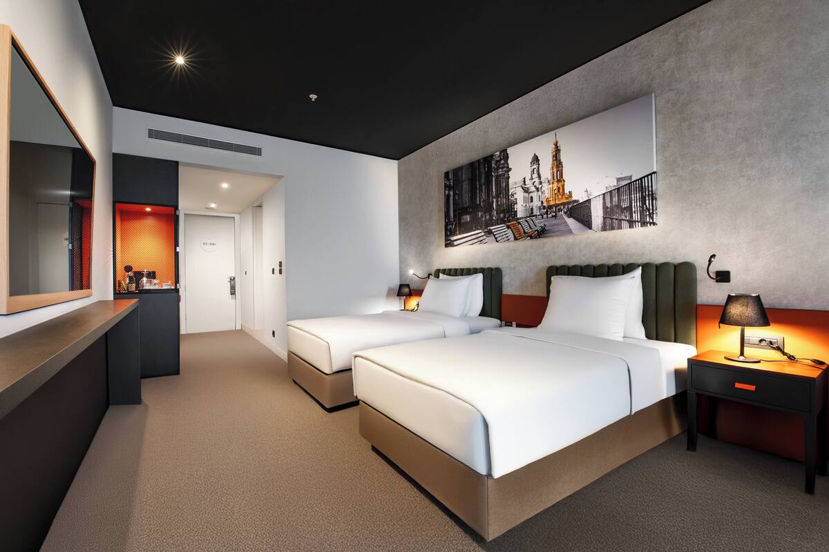 Une chambre d’hôtel moderne avec deux lits, un grand miroir, un bureau et une œuvre d’art accrochée au mur.