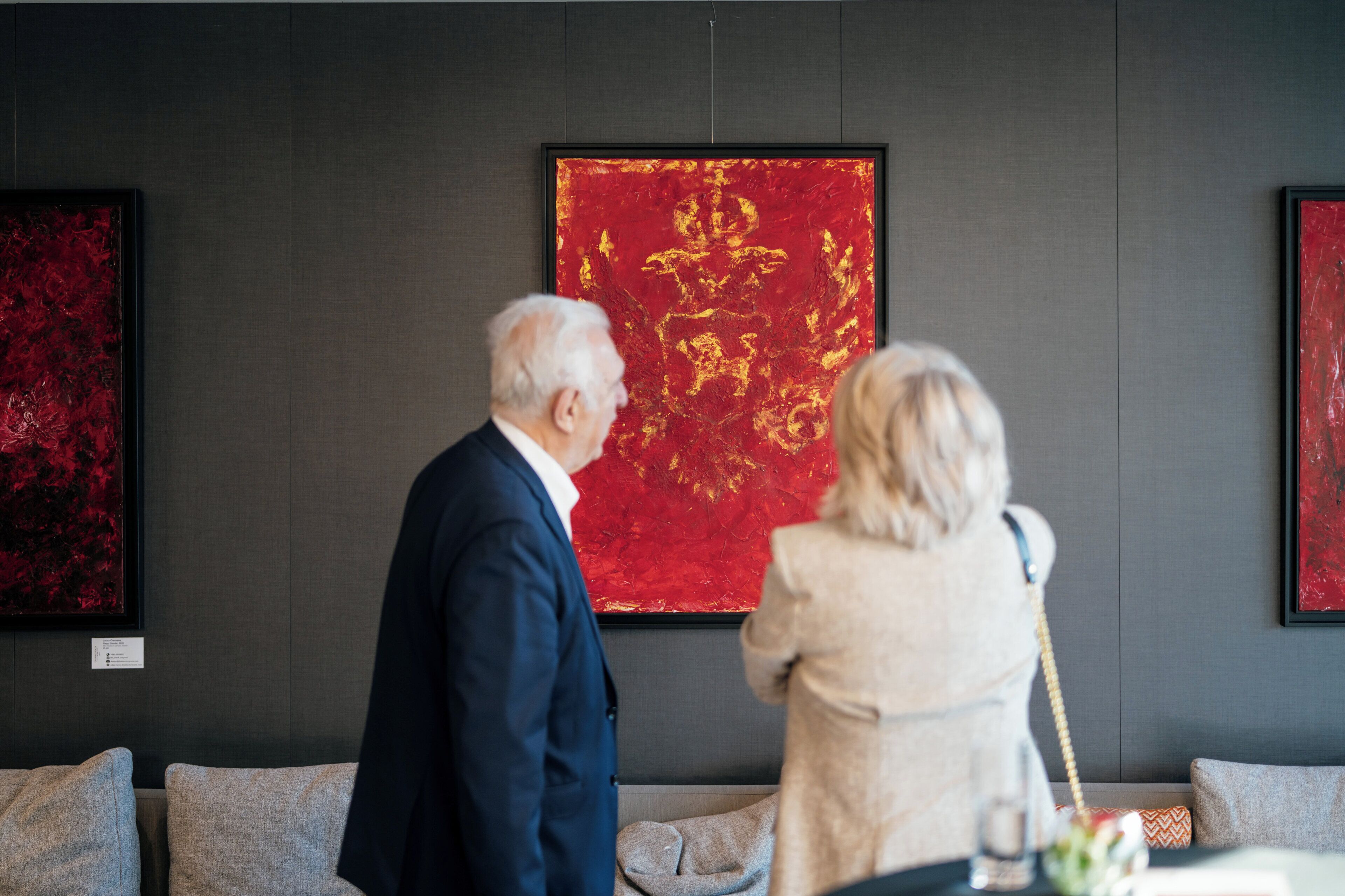 A room with a gray wall, a red artwork, and a gray sofa.