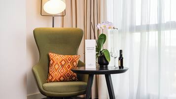 A green armchair with a patterned pillow, a small table with a wine bottle and glass, a potted orchid, and a sign reading 'FOOD FOR THOUGHT' in a hotel setting.