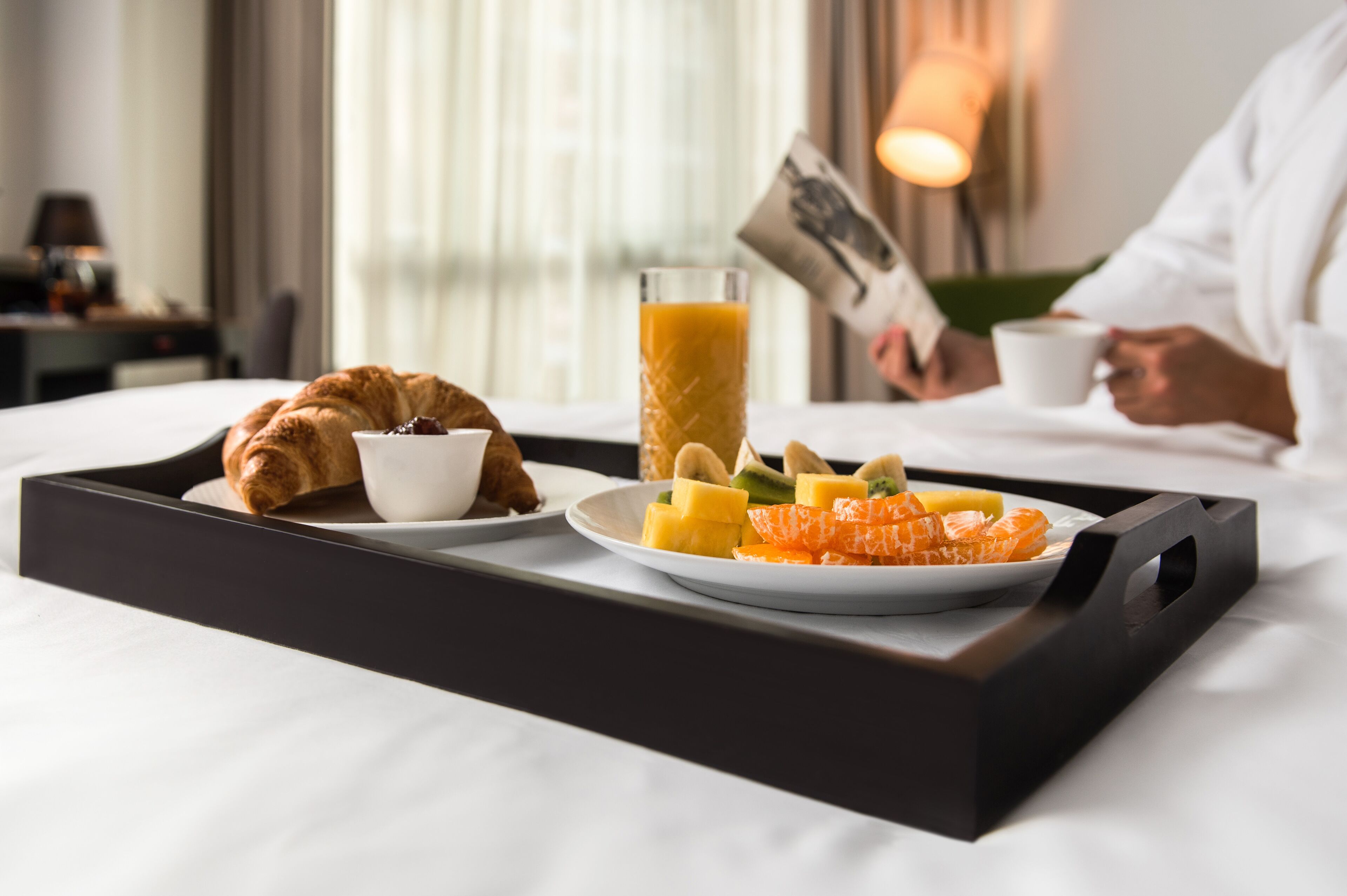 A breakfast tray with croissant, fruit, and juice on a bed.