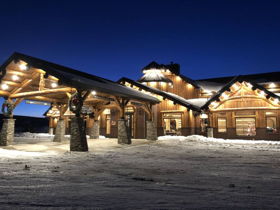 A large, well-lit lodge with multiple covered areas and stone pillars, surrounded by snow.