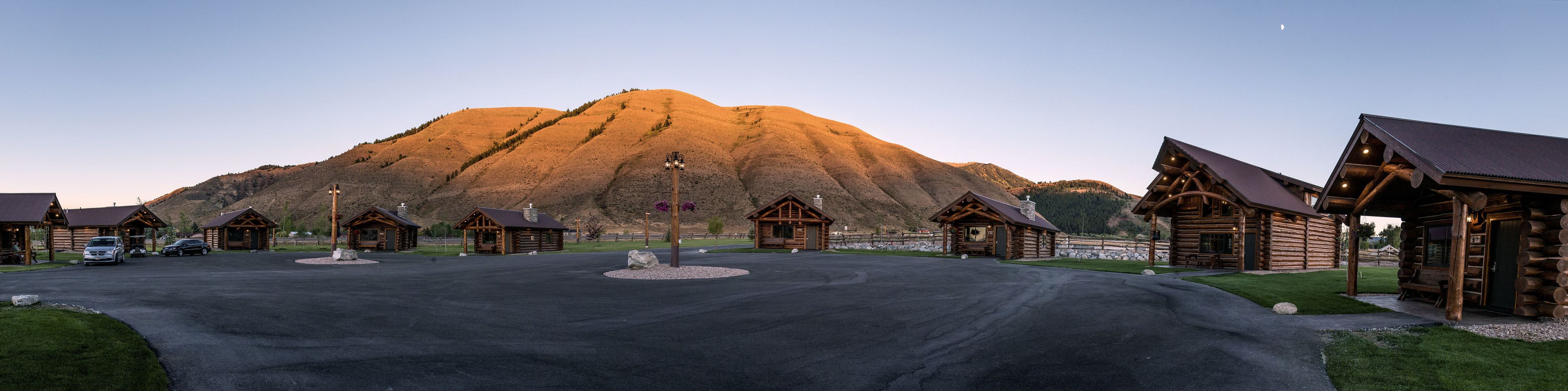 A log cabin resort with multiple cabins, a central building, and a mountain backdrop.