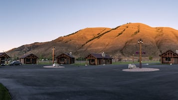 A log cabin resort with multiple cabins, a central building, and a mountain backdrop.
