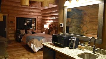 Una habitación tipo cabaña de madera con una cama, cafetera, lavamanos y chimenea de piedra.