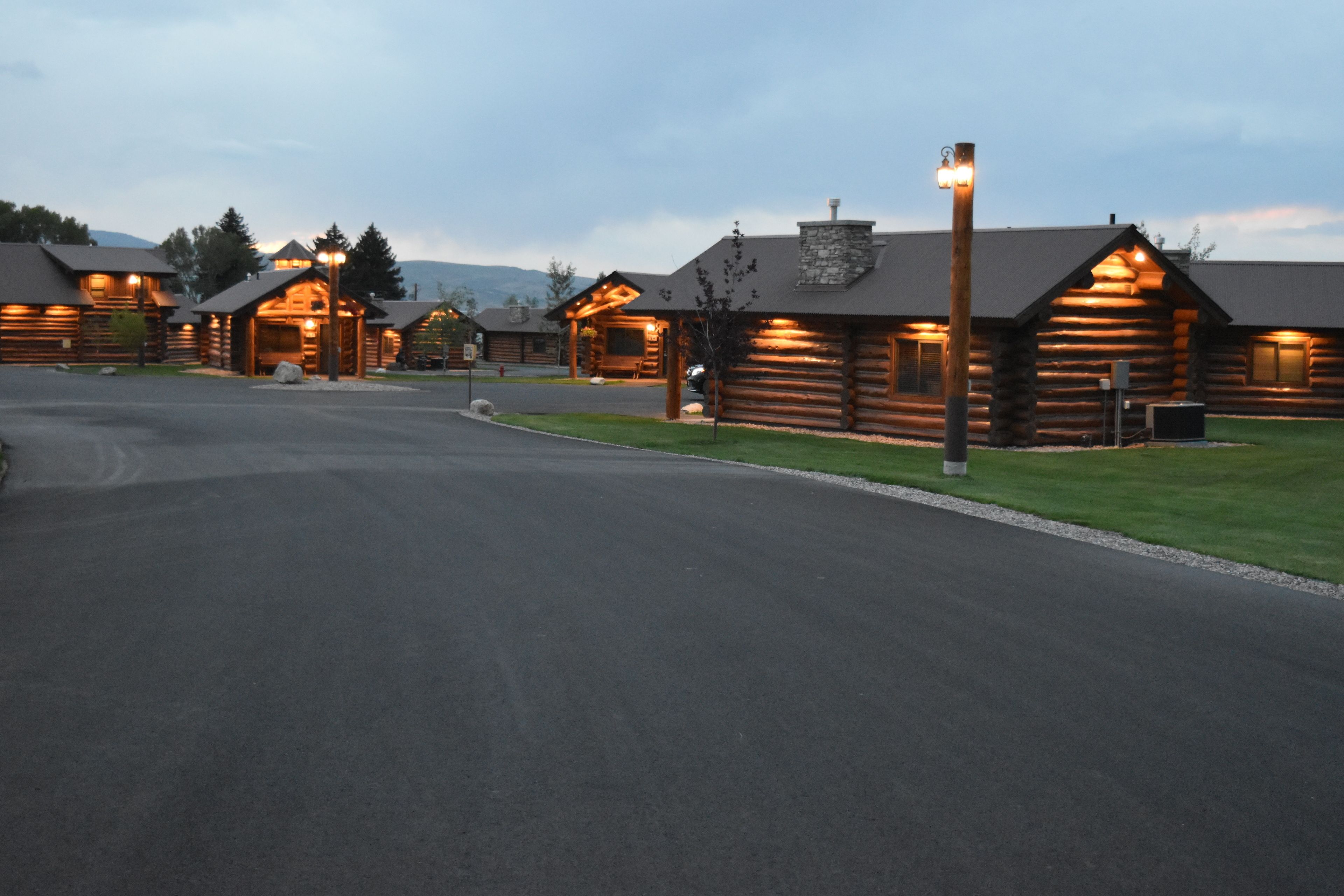 A row of log cabins with a paved driveway and well-maintained lawn.