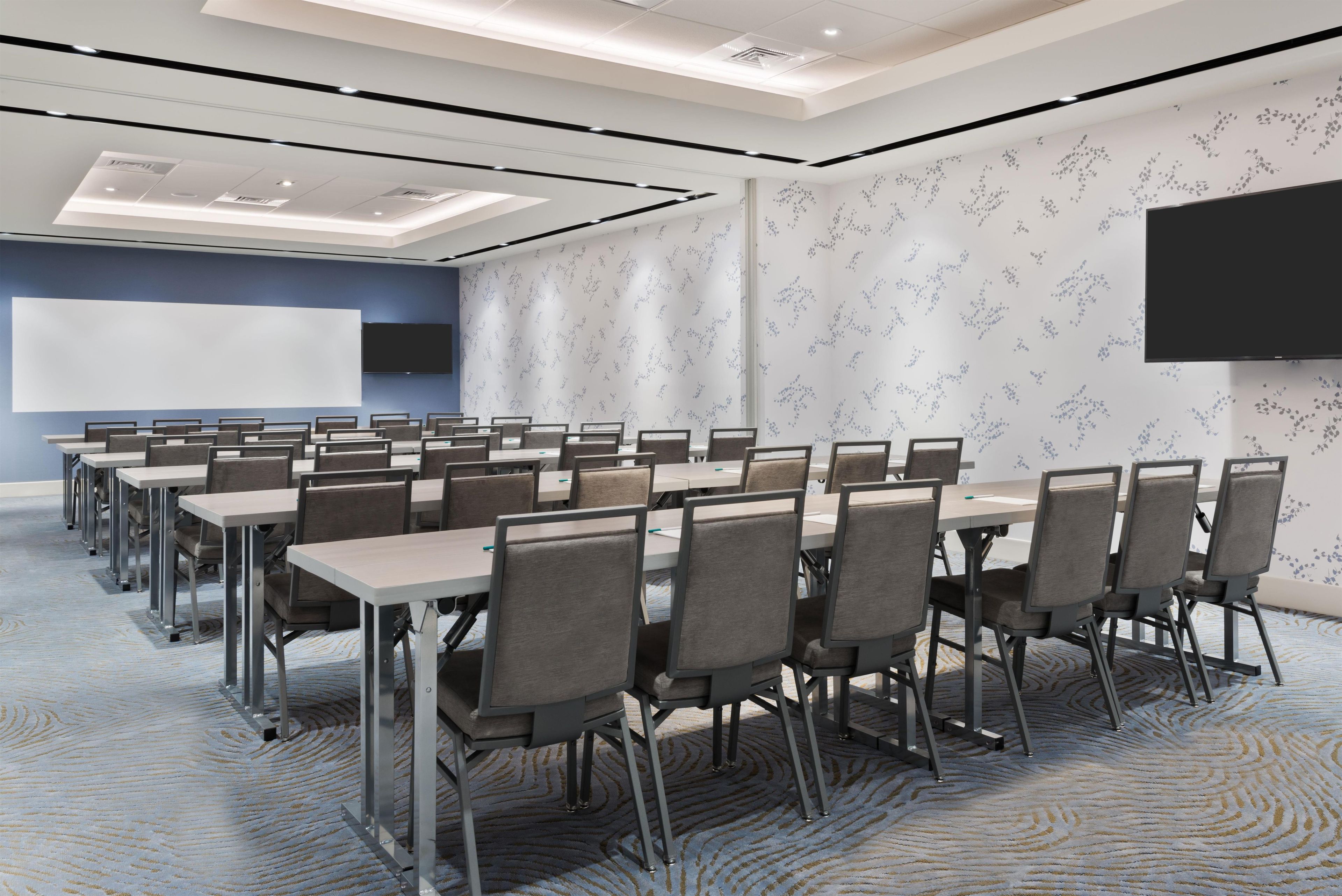 A conference room with a large screen, multiple tables, and chairs.