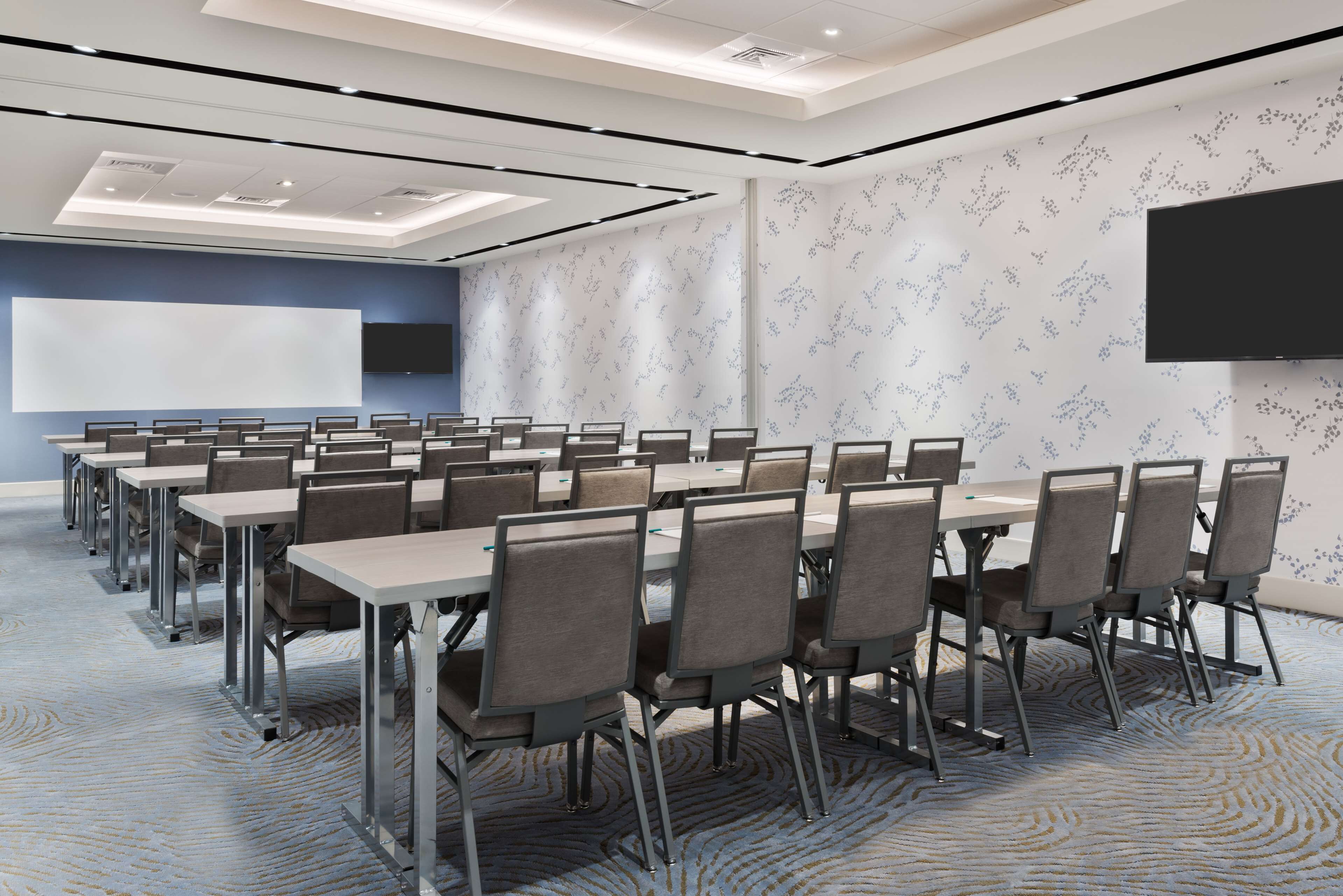 A conference room with multiple tables and chairs, a large screen, and a patterned carpet.