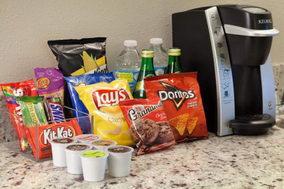 A kitchen counter with various snacks, including KitKat, Lay's, and Doritos, along with a Keurig coffee maker.