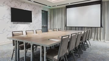 Una sala conferenze con un lungo tavolo, sedie, un televisore a schermo piatto, uno schermo per proiettore e carta da parati decorata.