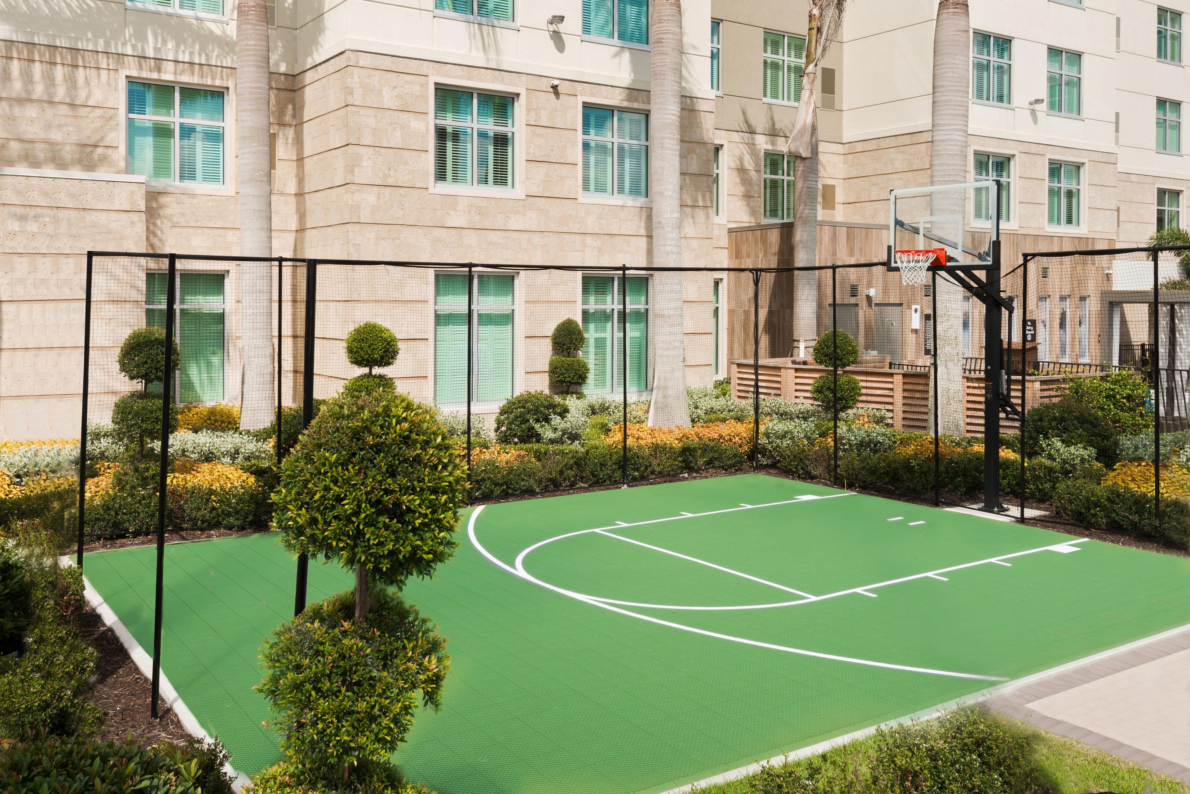 An outdoor basketball court surrounded by a fence, with a building in the background.