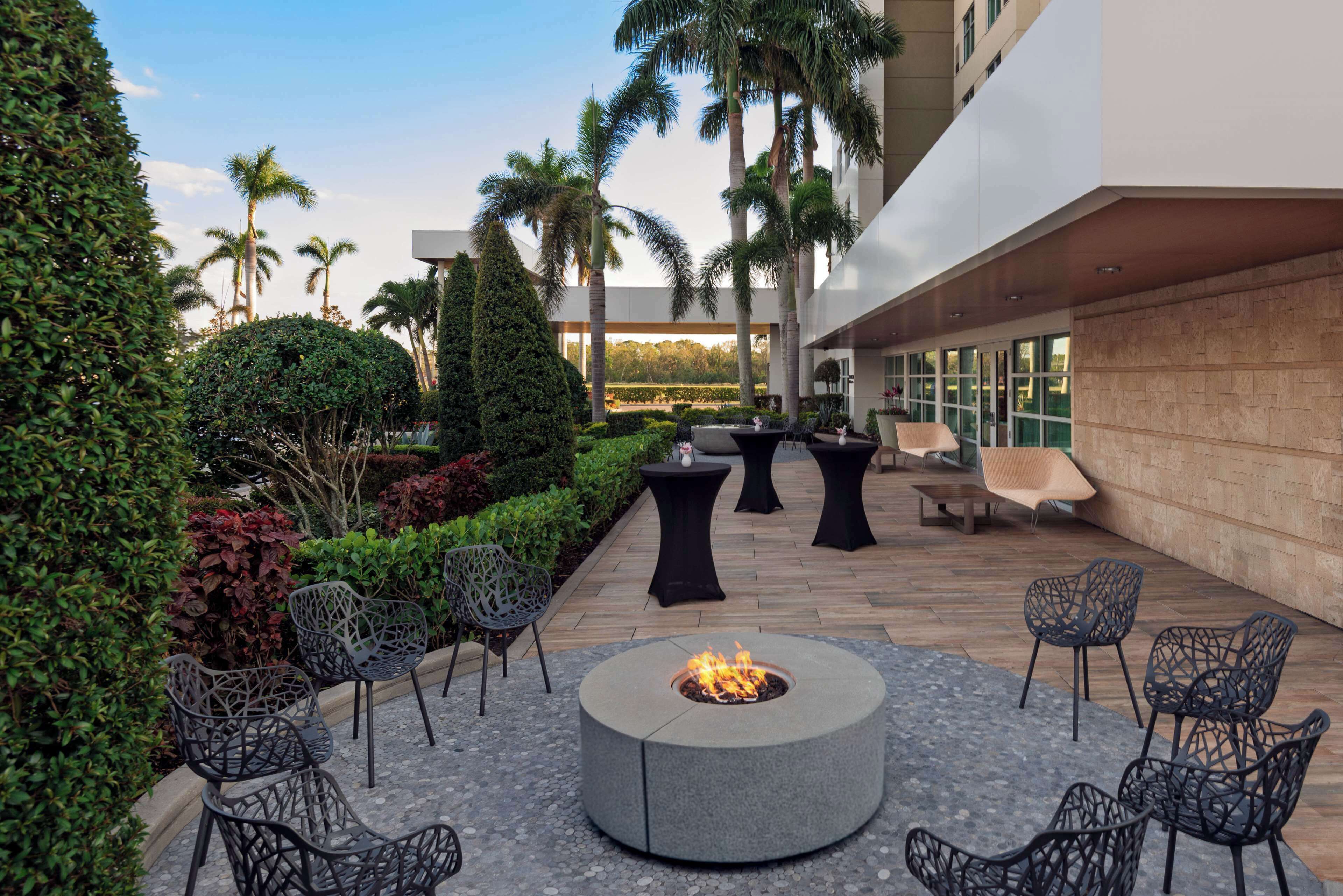 An outdoor patio with a fire pit, seating, and palm trees.