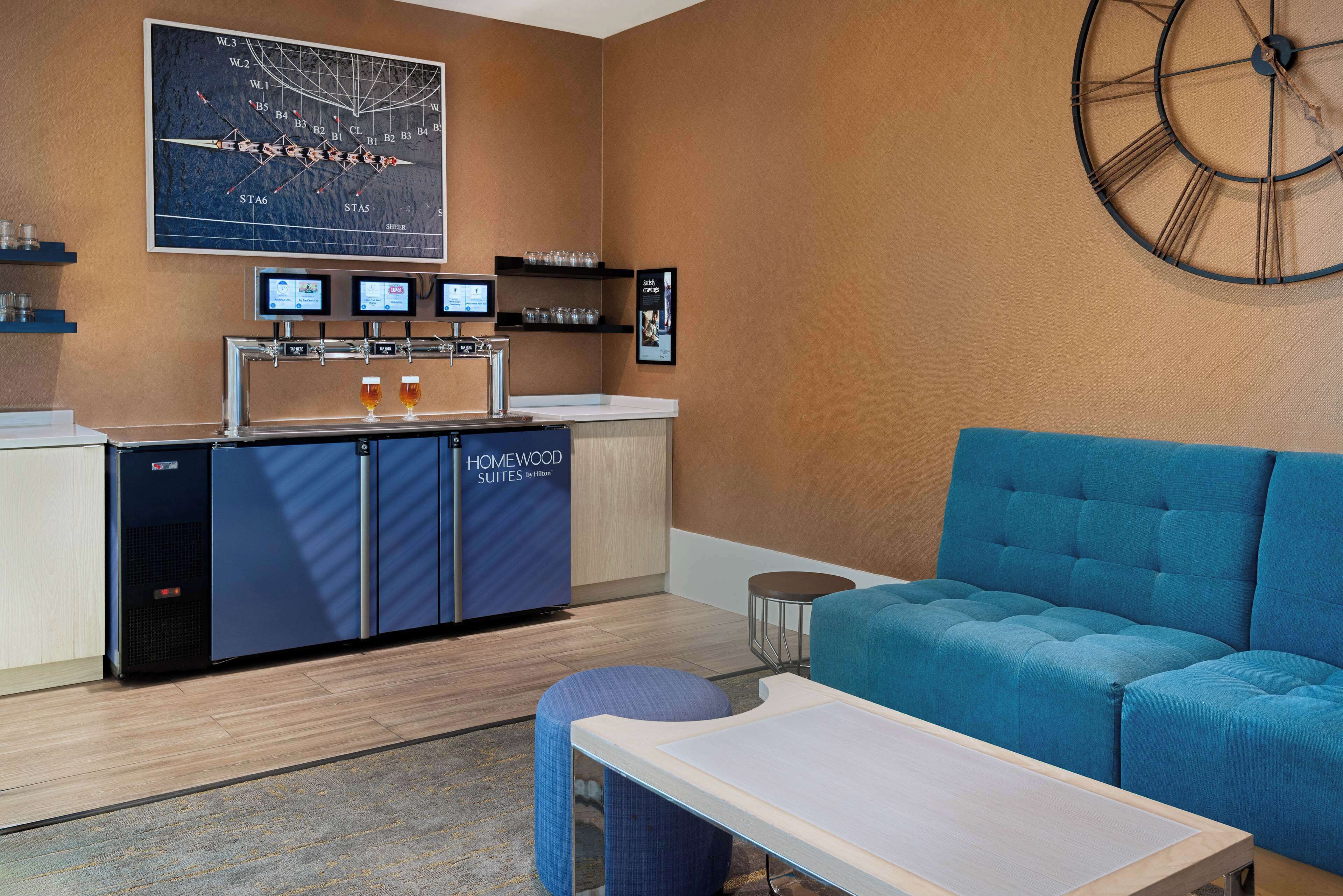A modern hotel room with a seating area, a minibar, and a large wall clock.