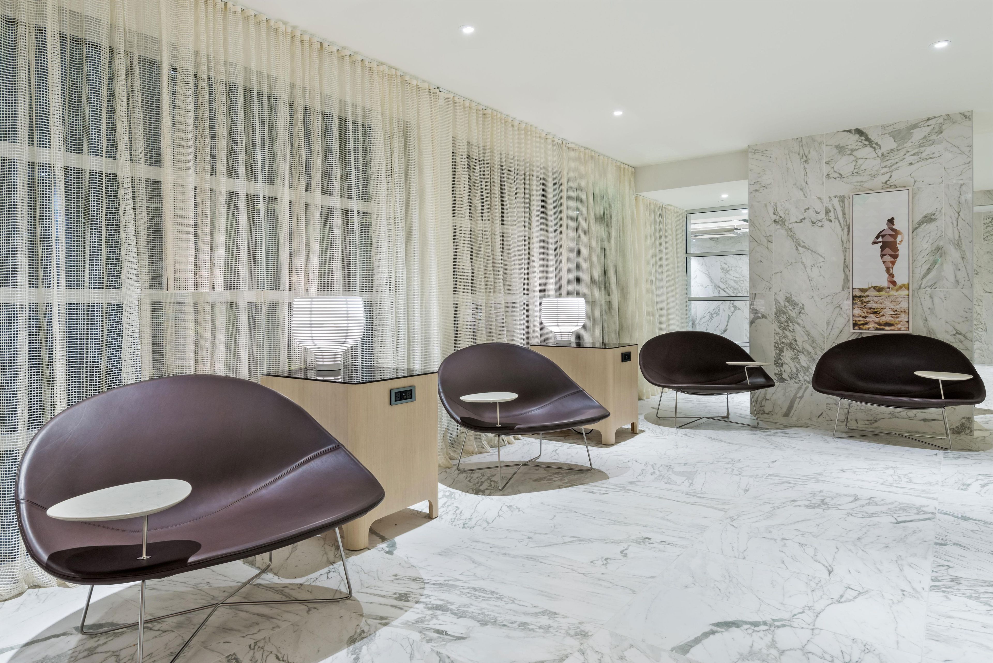 A modern interior with a reception desk, three black chairs, a patterned curtain, and marble flooring.