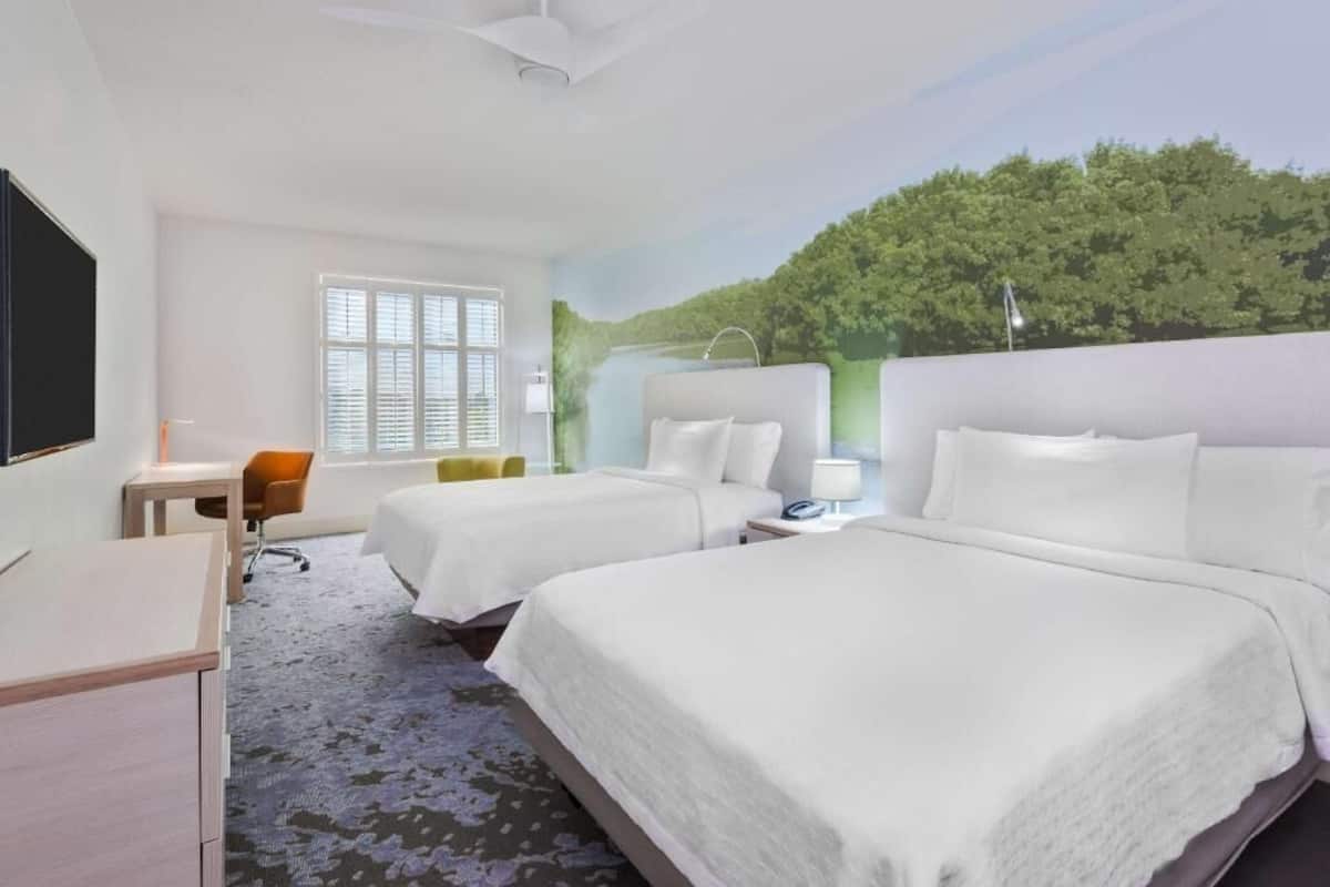 A hotel room with two beds, a desk, a chair, and a large window.
