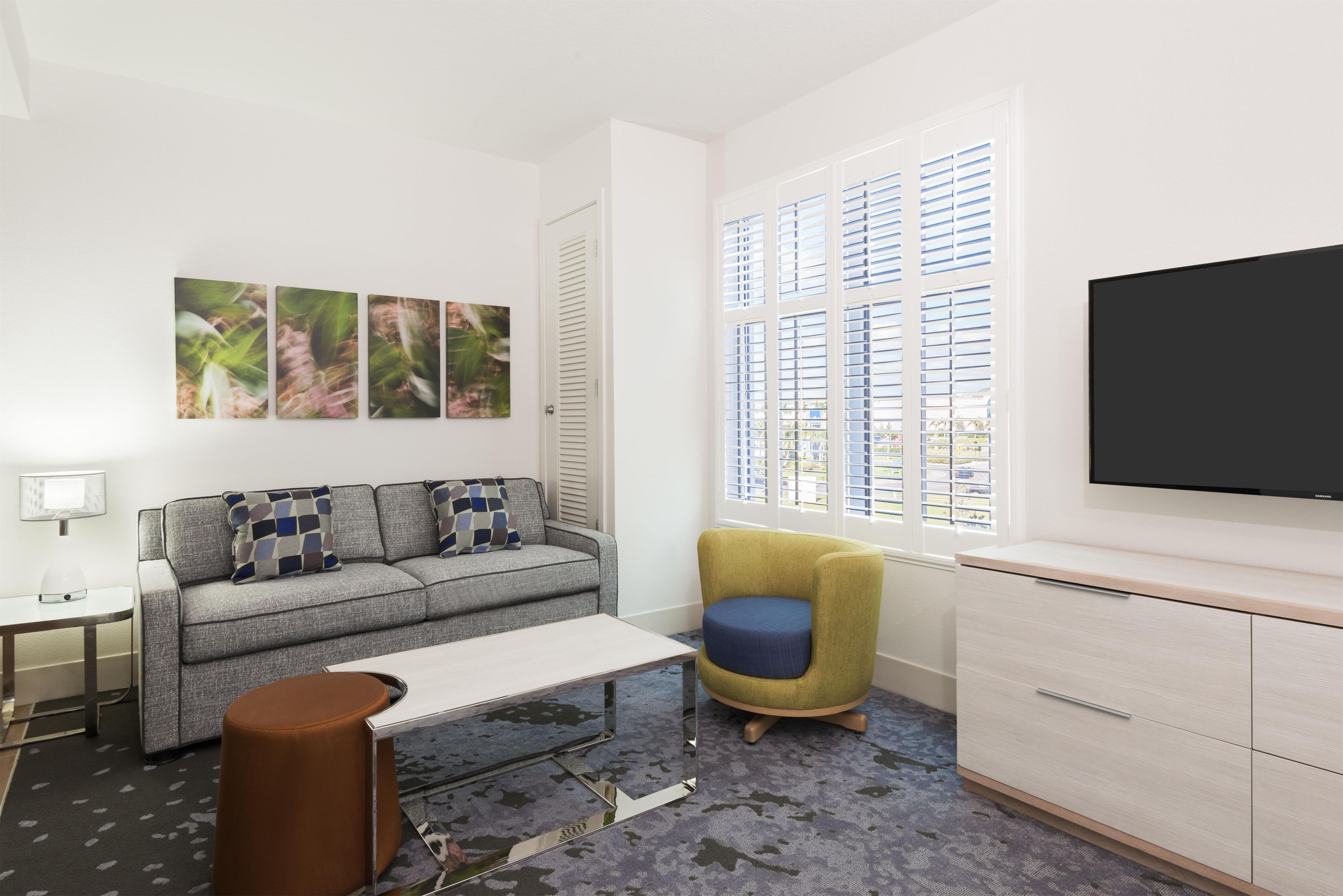 A modern living room with a sofa, a coffee table, a chair, a TV, and a window with blinds.