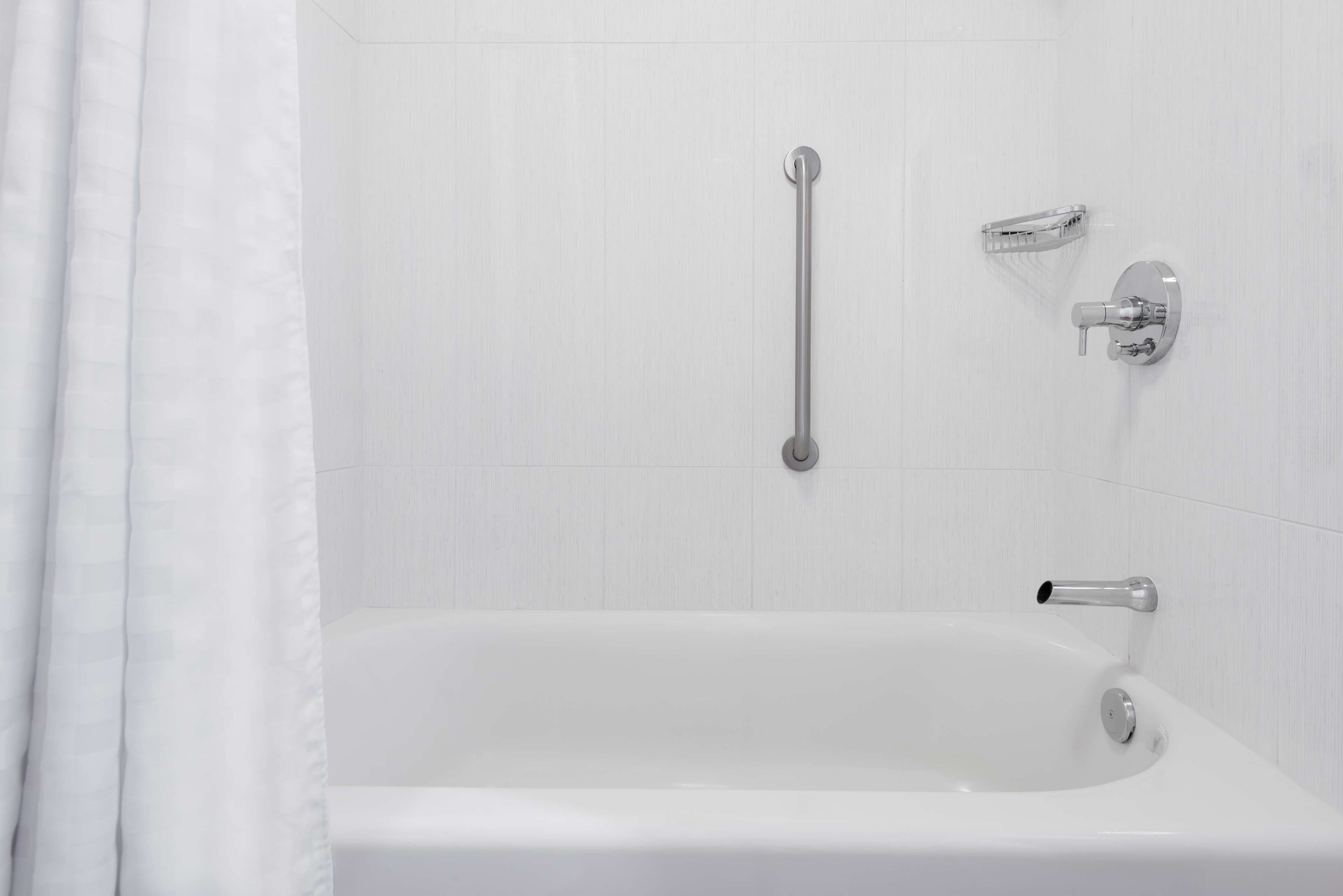 A white bathtub with a handheld showerhead, a grab bar, and a handheld showerhead mounted on the wall.