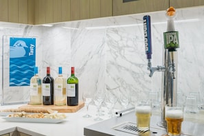 Un coin bar avec une tireuse à bière portant les inscriptions « BOD LIGHT » et « GOOSE IPA », une pancarte indiquant « Tasty » et plusieurs bouteilles de vin.