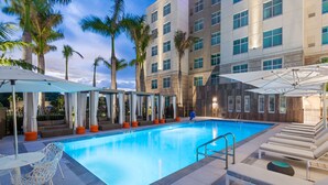 A swimming pool with lounge chairs and umbrellas, surrounded by palm trees and a multi-story building. - Homewood Suites by Hilton Sarasota Lakewood Ranch (Sarasota)