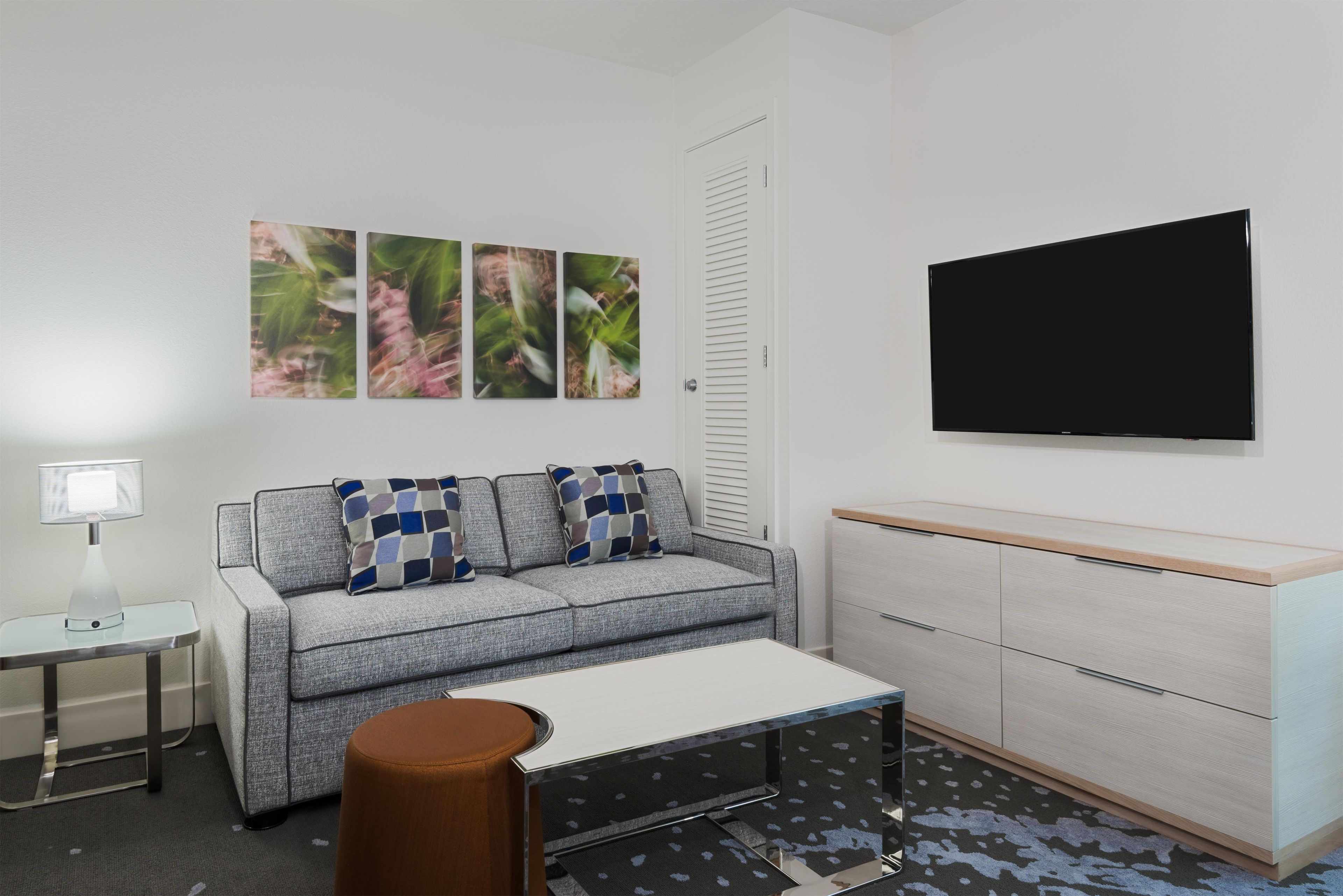 A modern living room with a grey sofa, patterned cushions, a coffee table, a TV, a side table, and a cabinet.