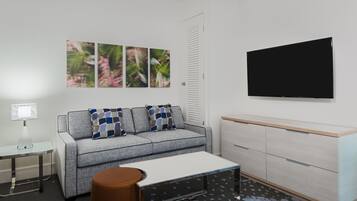 A modern living room with a grey sofa, patterned cushions, a coffee table, a TV, a side table, and a cabinet.