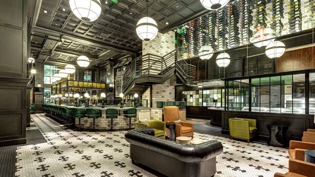 A modern interior with a black leather sofa, green and yellow chairs, and a patterned floor. - Hilton Norfolk The Main (Norfolk)