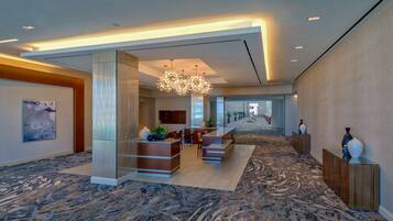 A spacious lobby with a central reception desk, seating area, and a chandelier.