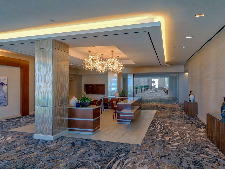 A spacious lobby with a central reception desk, seating area, and a chandelier.