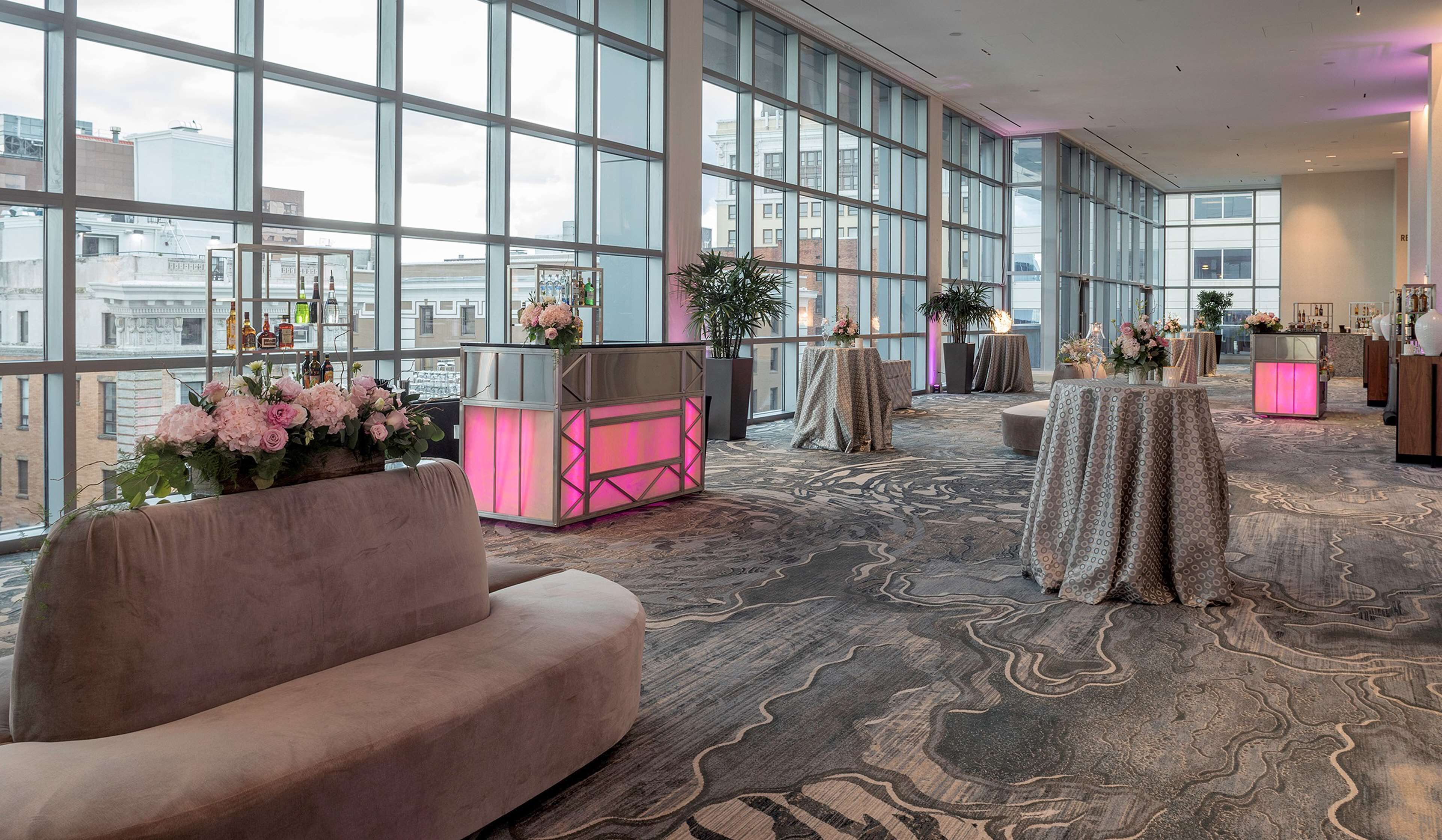 A spacious lobby with large windows, a plush sofa, and tables with floral arrangements.