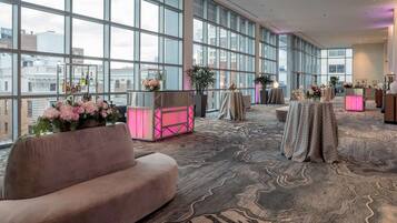 A spacious lobby with large windows, a plush sofa, and tables with floral arrangements.