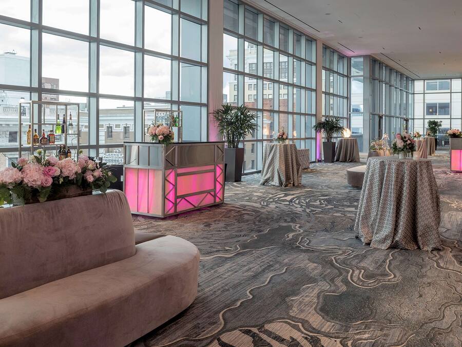A spacious lobby with large windows, a plush sofa, and tables with floral arrangements.