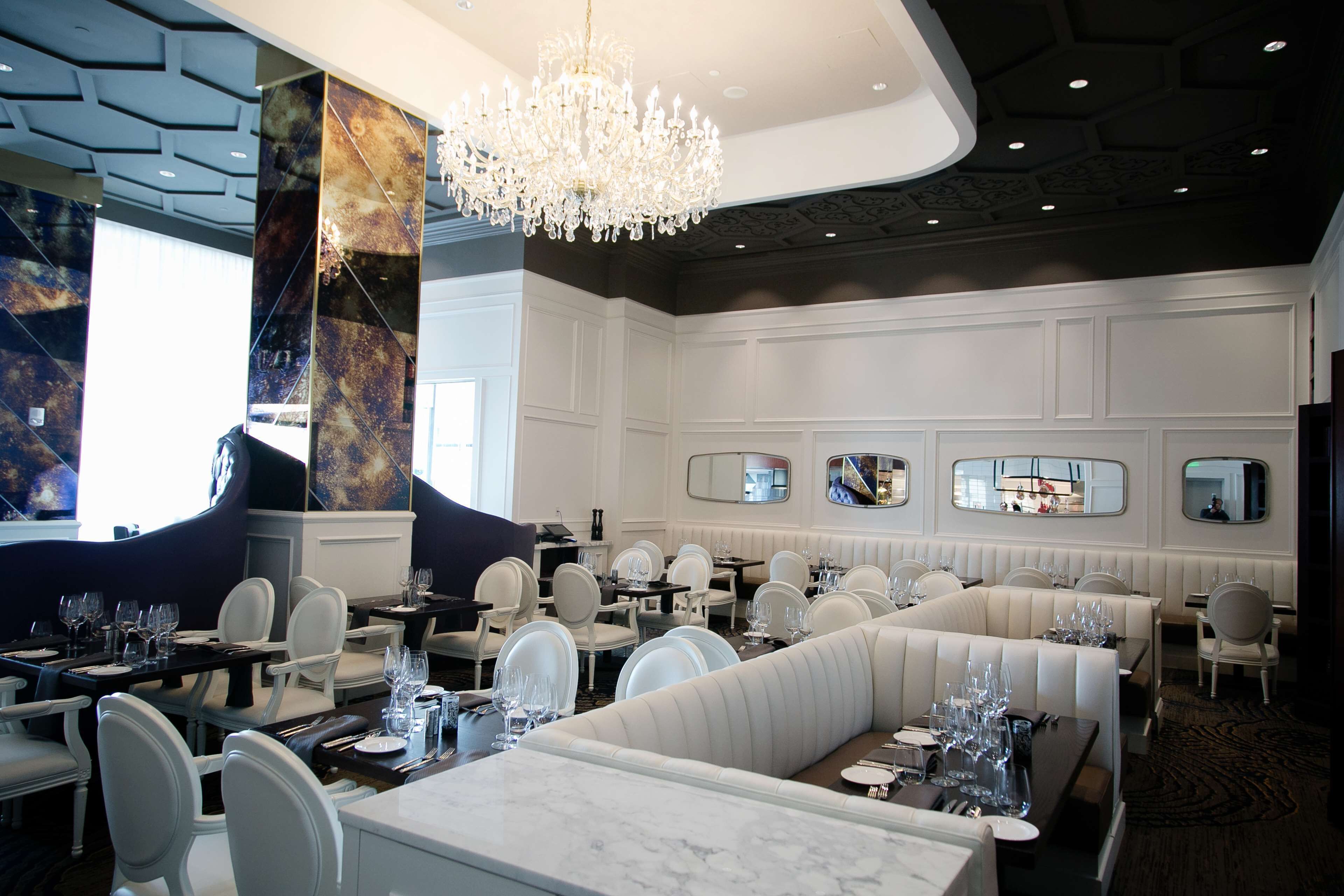 A restaurant with white booths, a large chandelier, and a modern ceiling design.