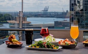 A table with various dishes and drinks, a glass of red wine, and a glass of orange juice, with a view of a river and buildings in the background.