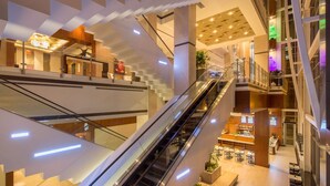 A multi-level interior with an escalator connecting floors, modern lighting, and a central seating area with tables and chairs. - Hilton Norfolk The Main (Norfolk)
