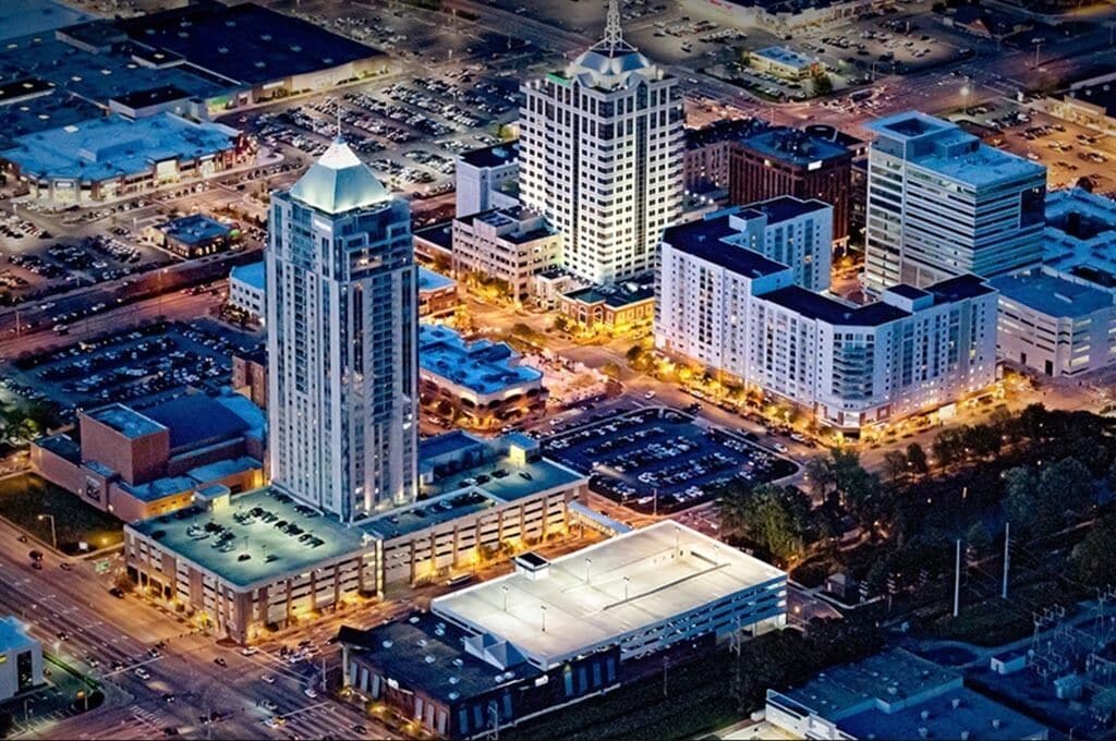 An aerial view of a cityscape with several high-rise buildings, a parking lot, and a large open area.