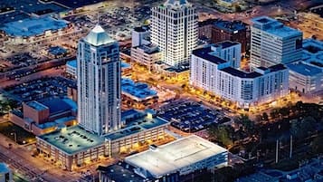 An aerial view of a cityscape with several high-rise buildings, a parking lot, and a large open area.