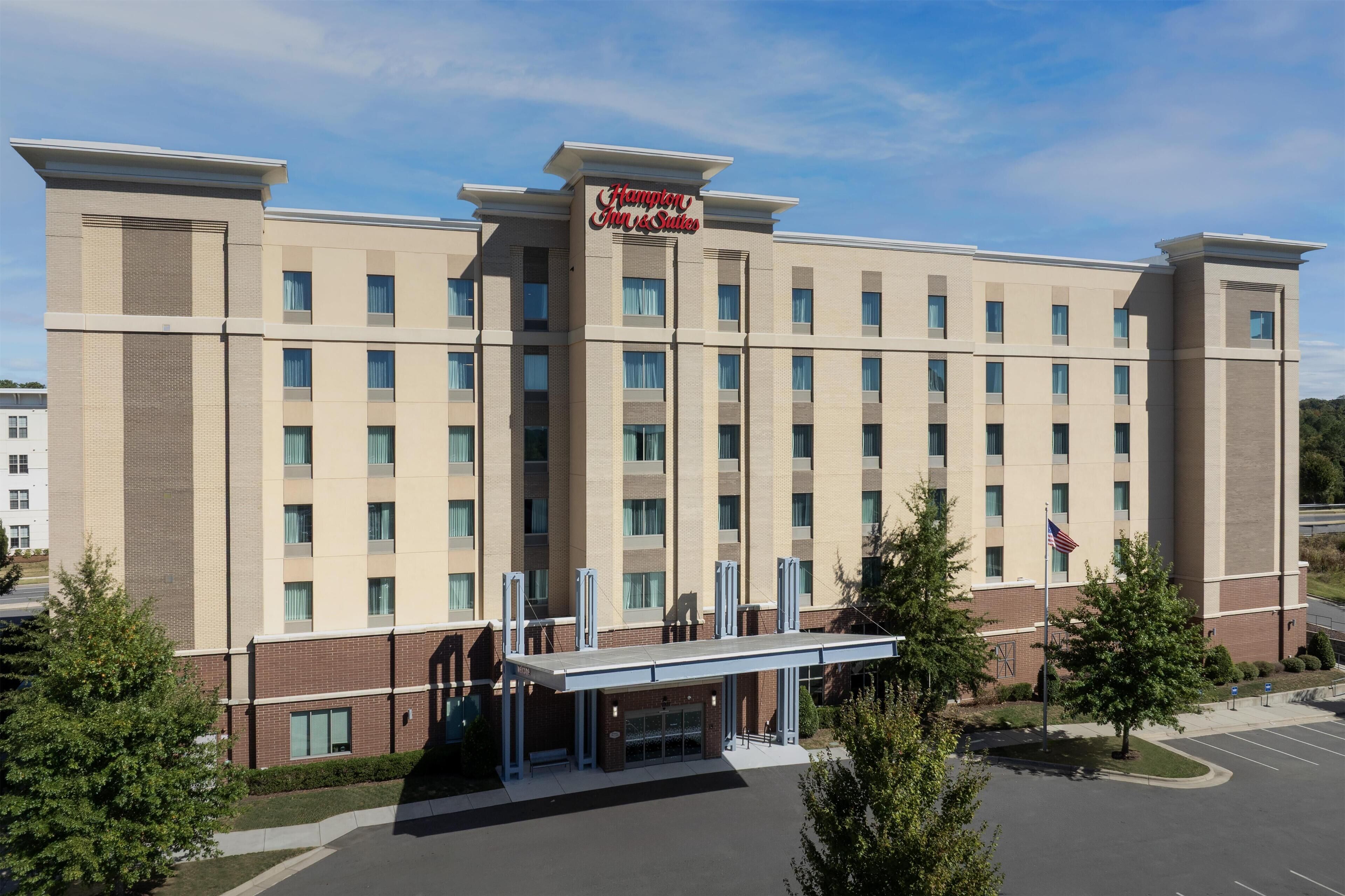 Un grand hôtel à plusieurs étages, reconnaissable à son enseigne bien visible indiquant « Hampton Inn & Suites ».