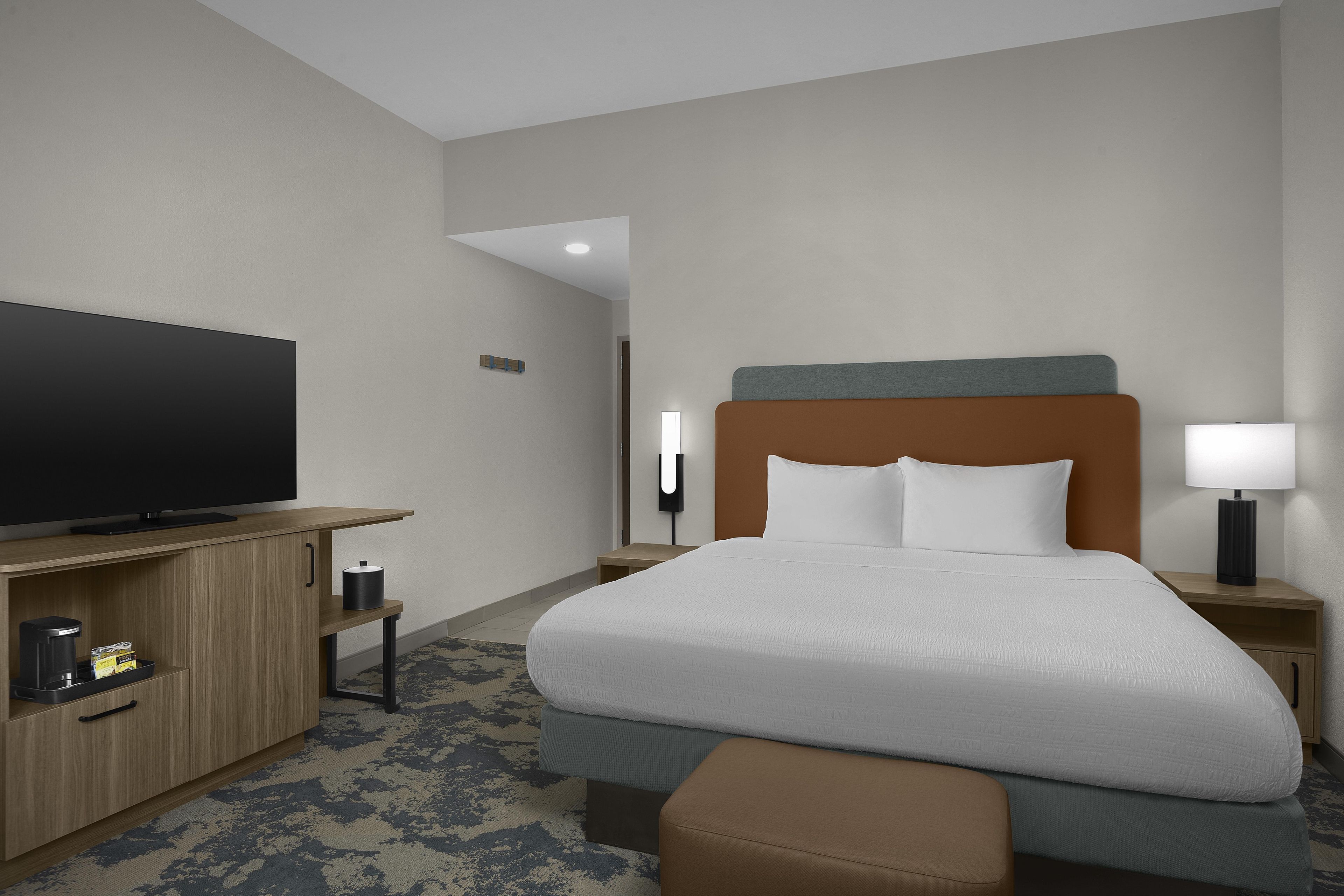 A hotel room with a bed, a television, a nightstand, a lamp, and a coffee maker.