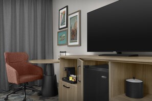 A hotel room with a modern desk, a comfortable armchair, a television, and a trash bin. - Hampton Inn & Suites Charlotte/Ballantyne (Charlotte)