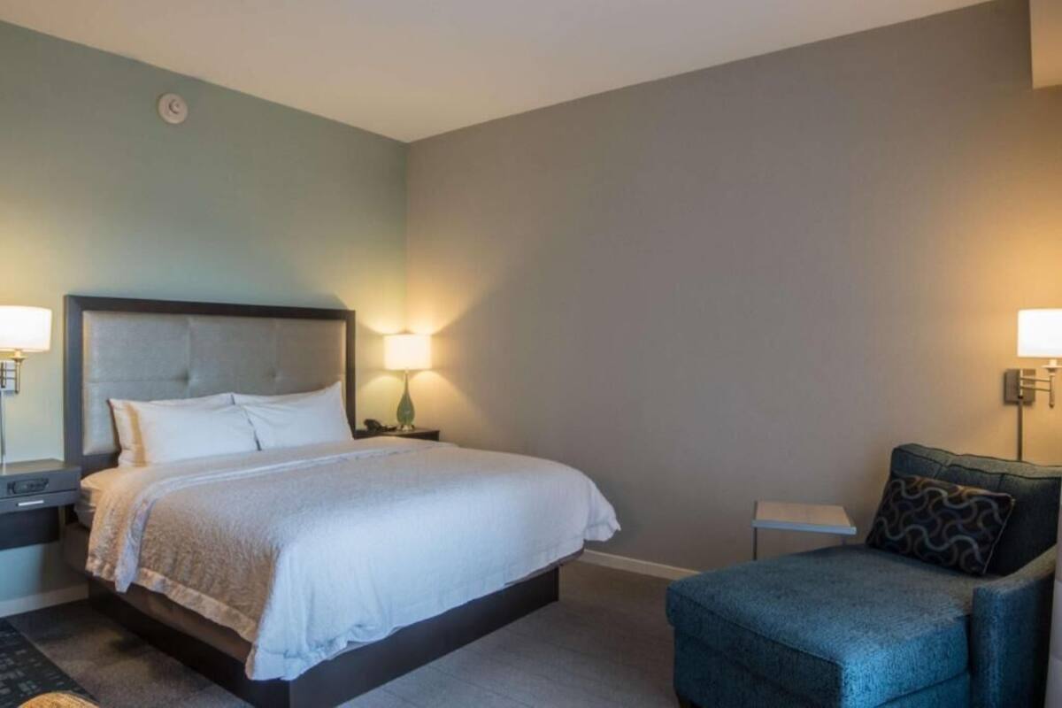 A bedroom with a bed, bedside tables, a chair, and wall-mounted lamps.