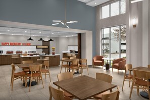 A modern breakfast area with a central counter, seating arrangements, and a large window providing a view. - Hampton Inn & Suites Charlotte/Ballantyne (Charlotte)