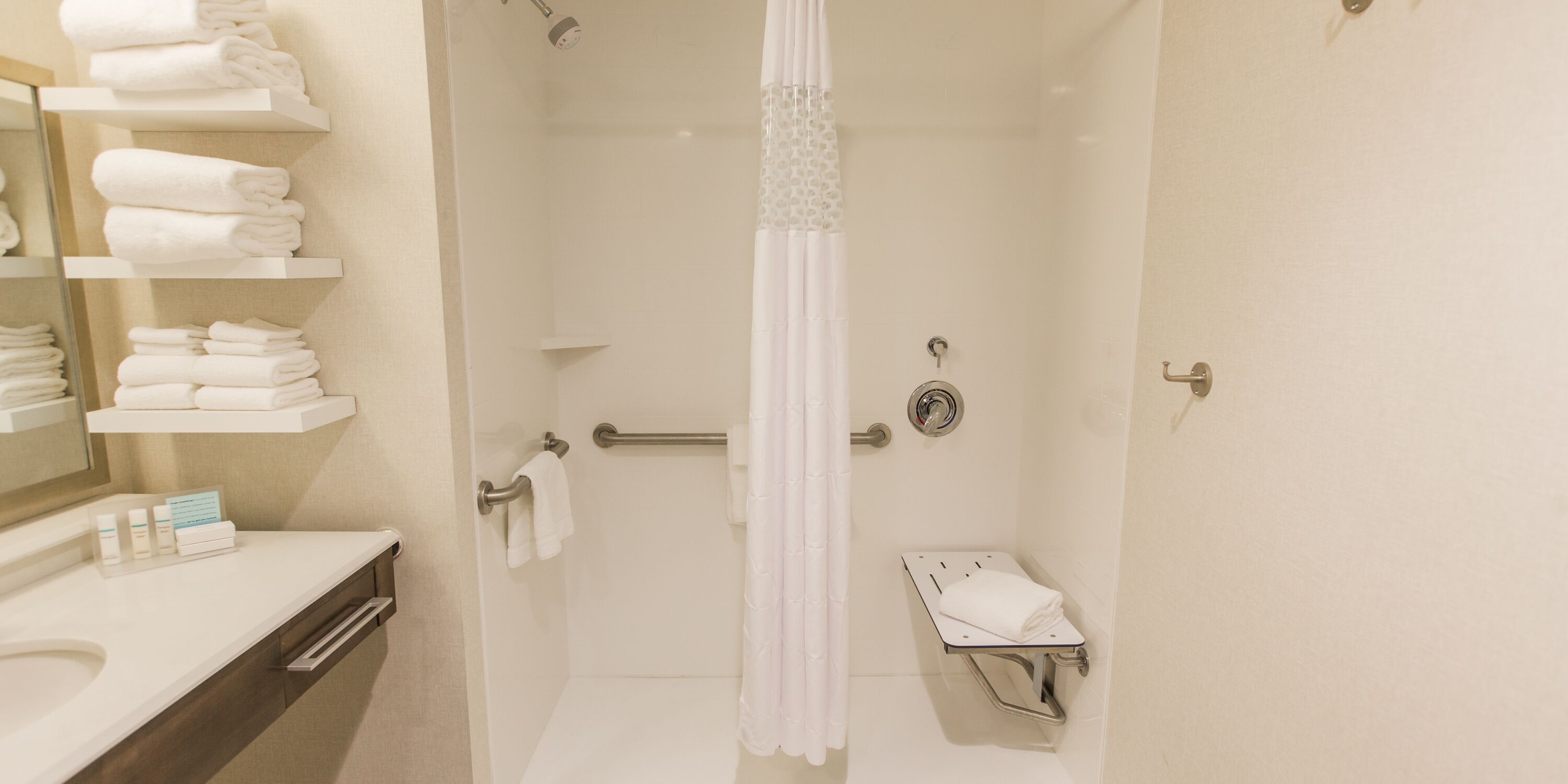 Une salle de bain moderne équipée d’une douche, de toilettes et d’un lavabo. On y trouve des étagères avec des serviettes pliées et des articles de toilette.
