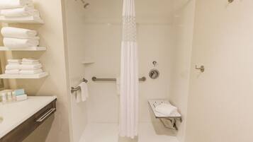 A modern bathroom with a shower, a toilet, and a sink. There are shelves with folded towels and toiletries.
