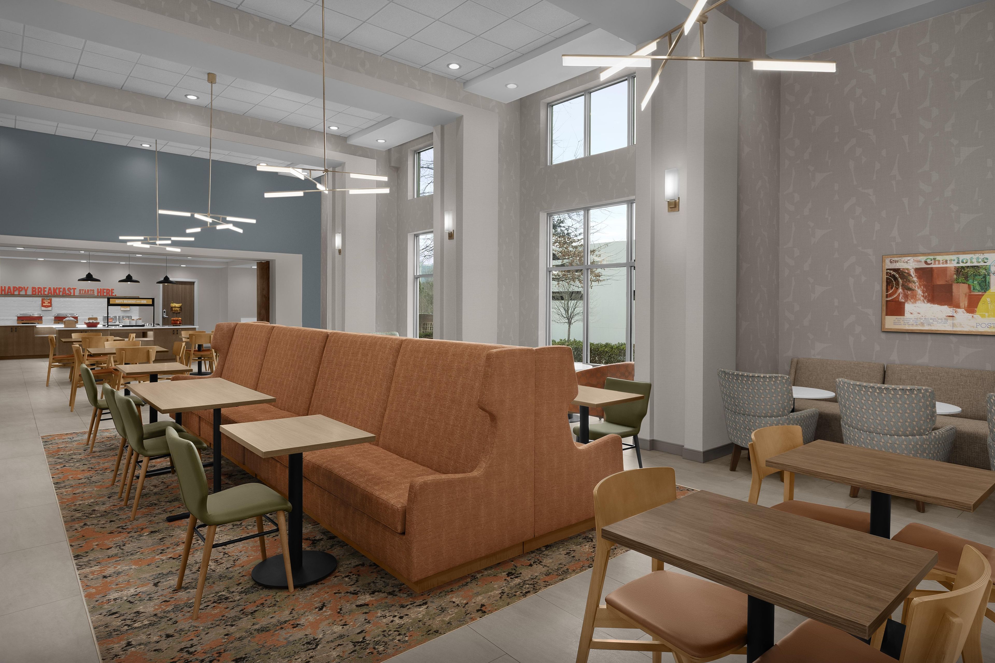 Een moderne eetruimte met een centrale oranje bank, meerdere tafels en stoelen.
