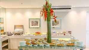 A buffet with various food items and a tall floral centerpiece. - Céu Palmas Hotel (Palmas)