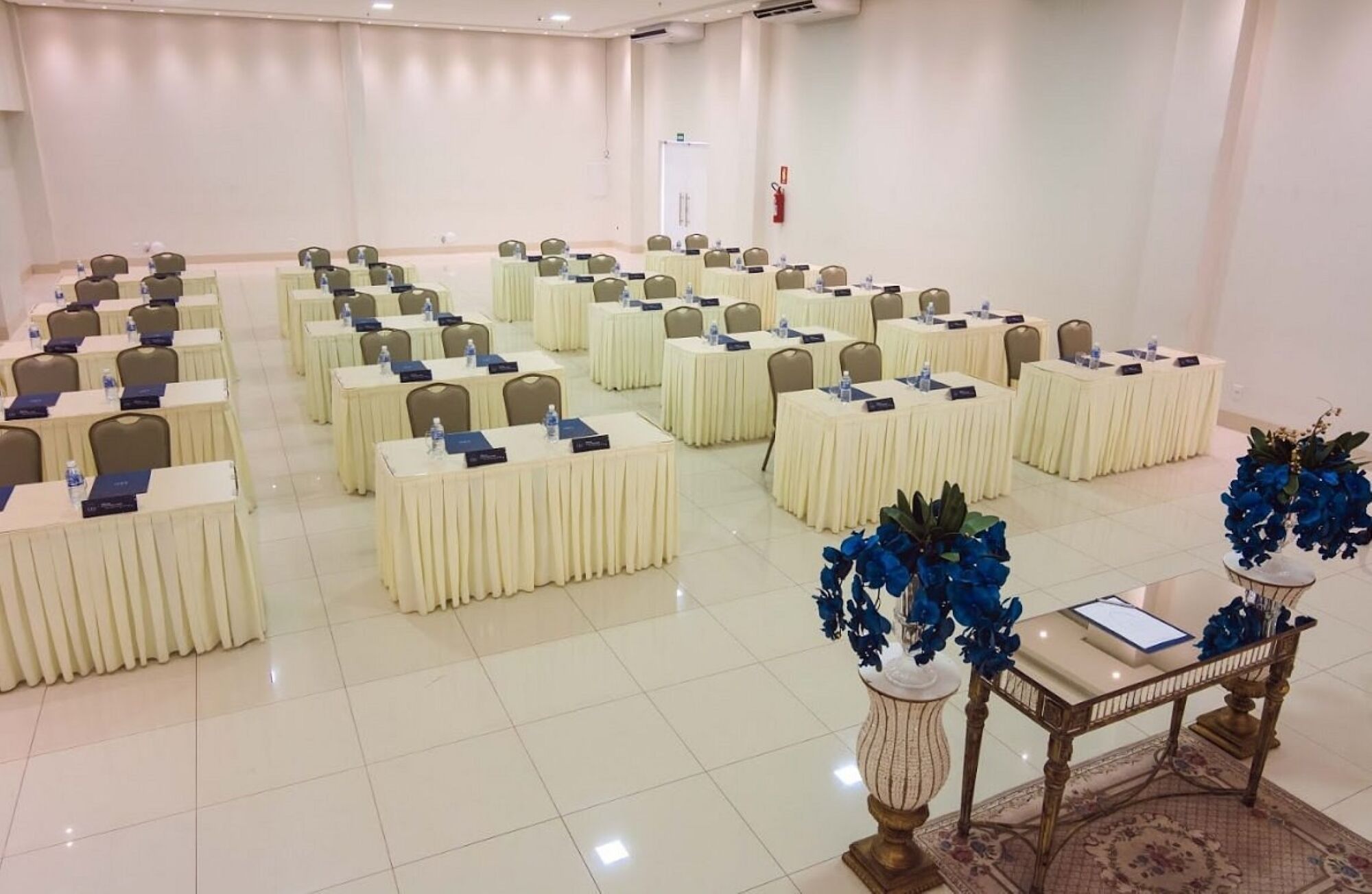 Une salle de conférence avec des rangées de tables et de chaises, un tableau blanc et un extincteur fixé au mur.