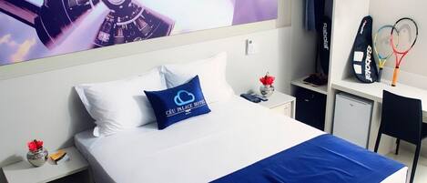 Habitación de hotel con cama, mesita de noche, escritorio y silla. Un televisor montado en la pared muestra una imagen con temática espacial.