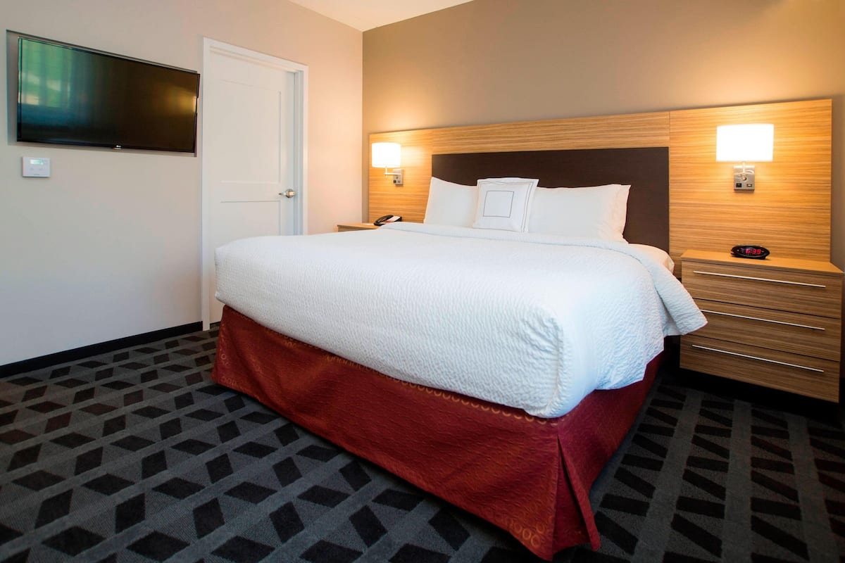 A hotel room with a bed, bedside tables, a TV, and a wall-mounted light.